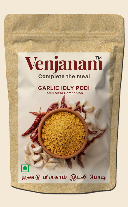 Venjanam Garlic Idly Podi packaging with yellow powder, red chilies, and white onions on a beige background.